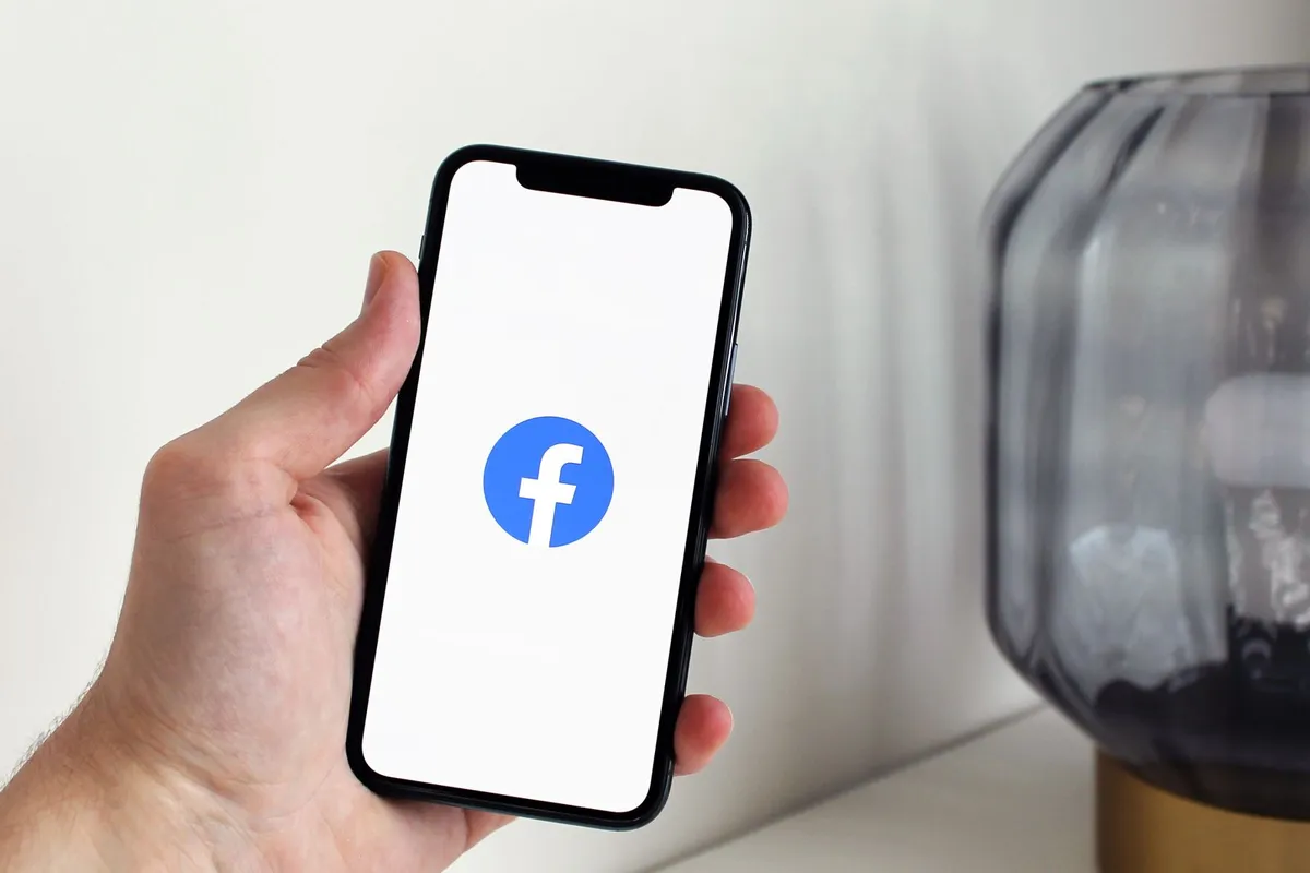 En person holder en mobil med Facebook-appen åpen.