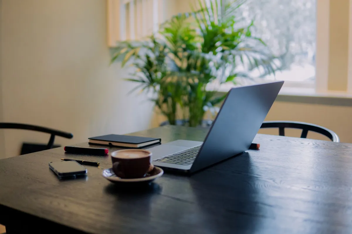 Lyst arbeidsbord med laptop, kaffe og en grønn plante i et studio i Oslo.
