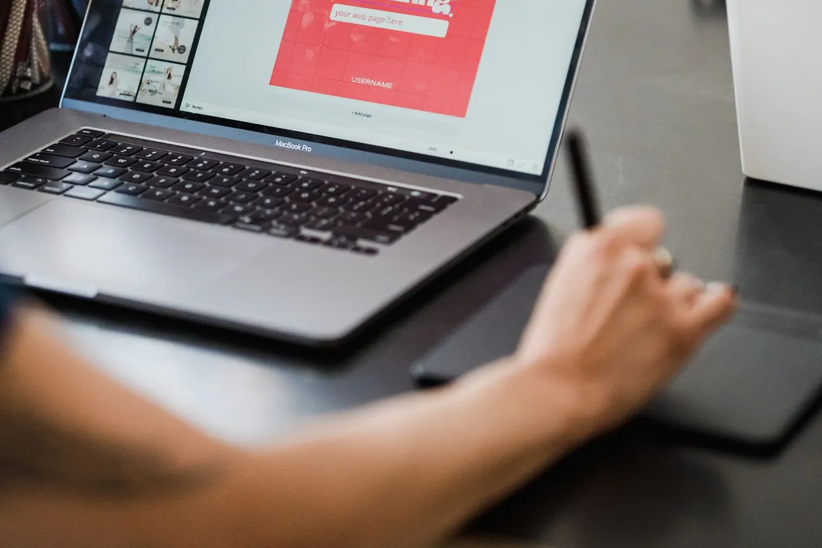 Designer som jobber med tegnebrett og laptop med et nettsidedesign på skjermen.