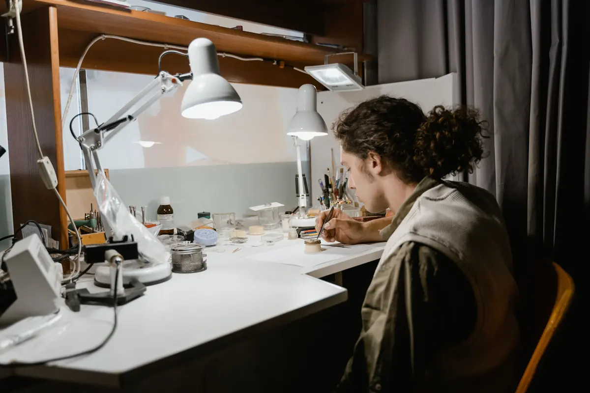 En urmaker bøyd over arbeidsbenken under en lampe, omgitt av små deler og presisjonsverktøy.
