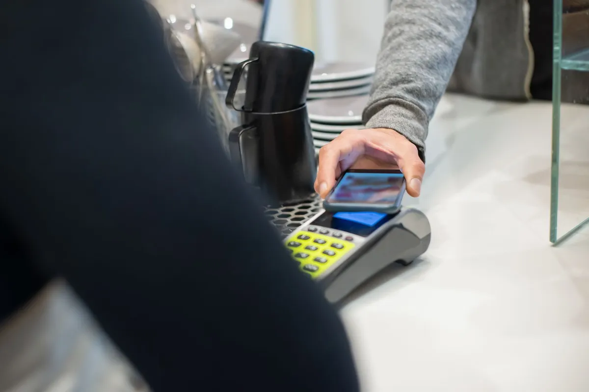 En kunde betaler kontaktløst med mobilen på en kafé.